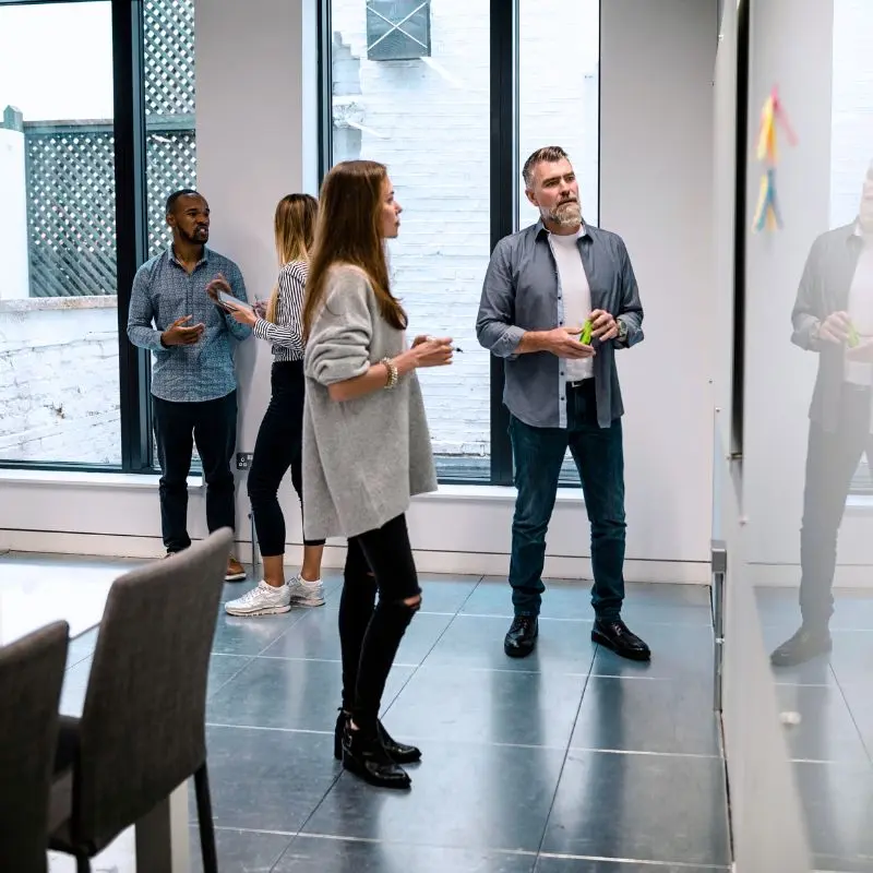 Un groupe d’adultes en discussion informelle devant un tableau blanc. Illustration d’une formation non structurée avec peu d’encadrement pédagogique.