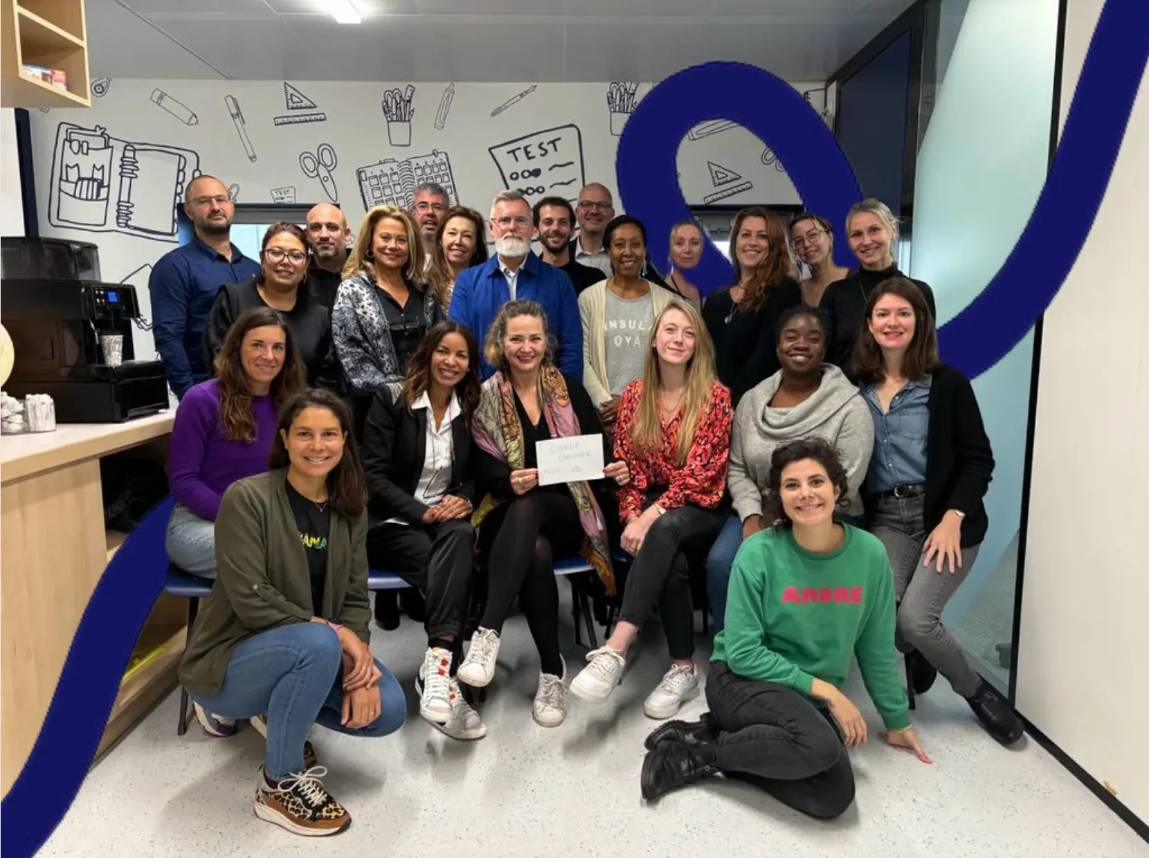 Group of professionals sitting on the floor in a training room, smiling and gesturing enthusiastically after an immersive management workshop.