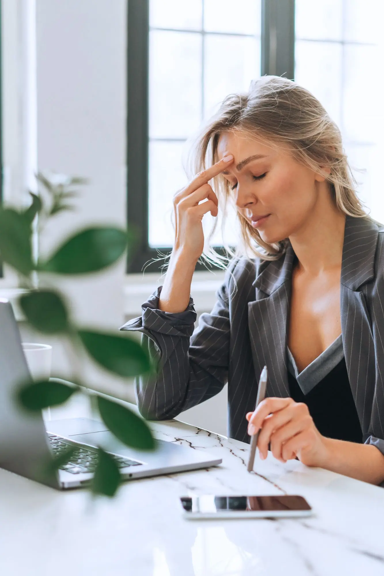 Femme en costume, visiblement stressée, les yeux fermés et la main sur le front devant son ordinateur. Illustration du manque de suivi post-formation et de ses conséquences sur les managers.
