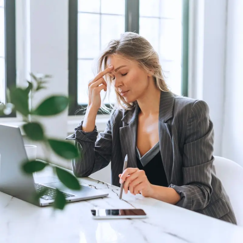 Femme en costume, visiblement stressée, les yeux fermés et la main sur le front devant son ordinateur. Illustration du manque de suivi post-formation et de ses conséquences sur les managers.